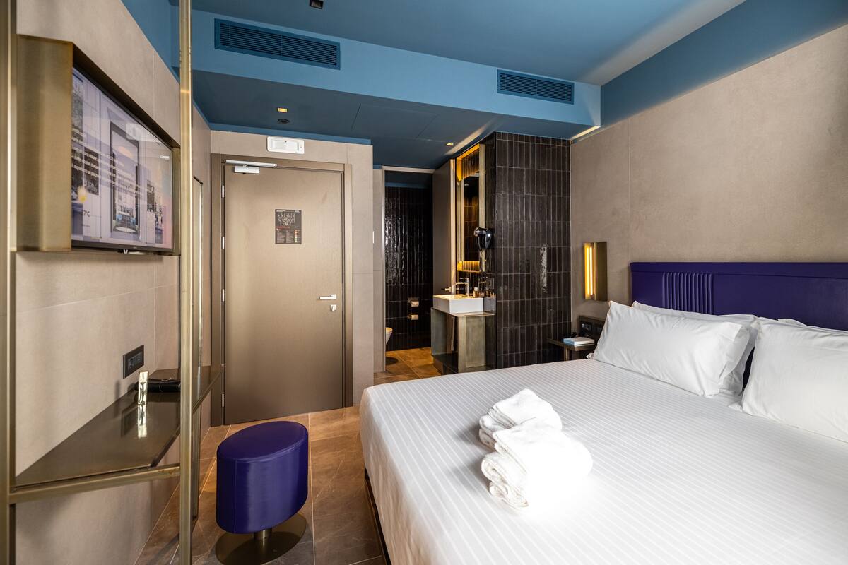 A hotel room with a large bed, a bathroom with a mirror, and a TV mounted on the wall.