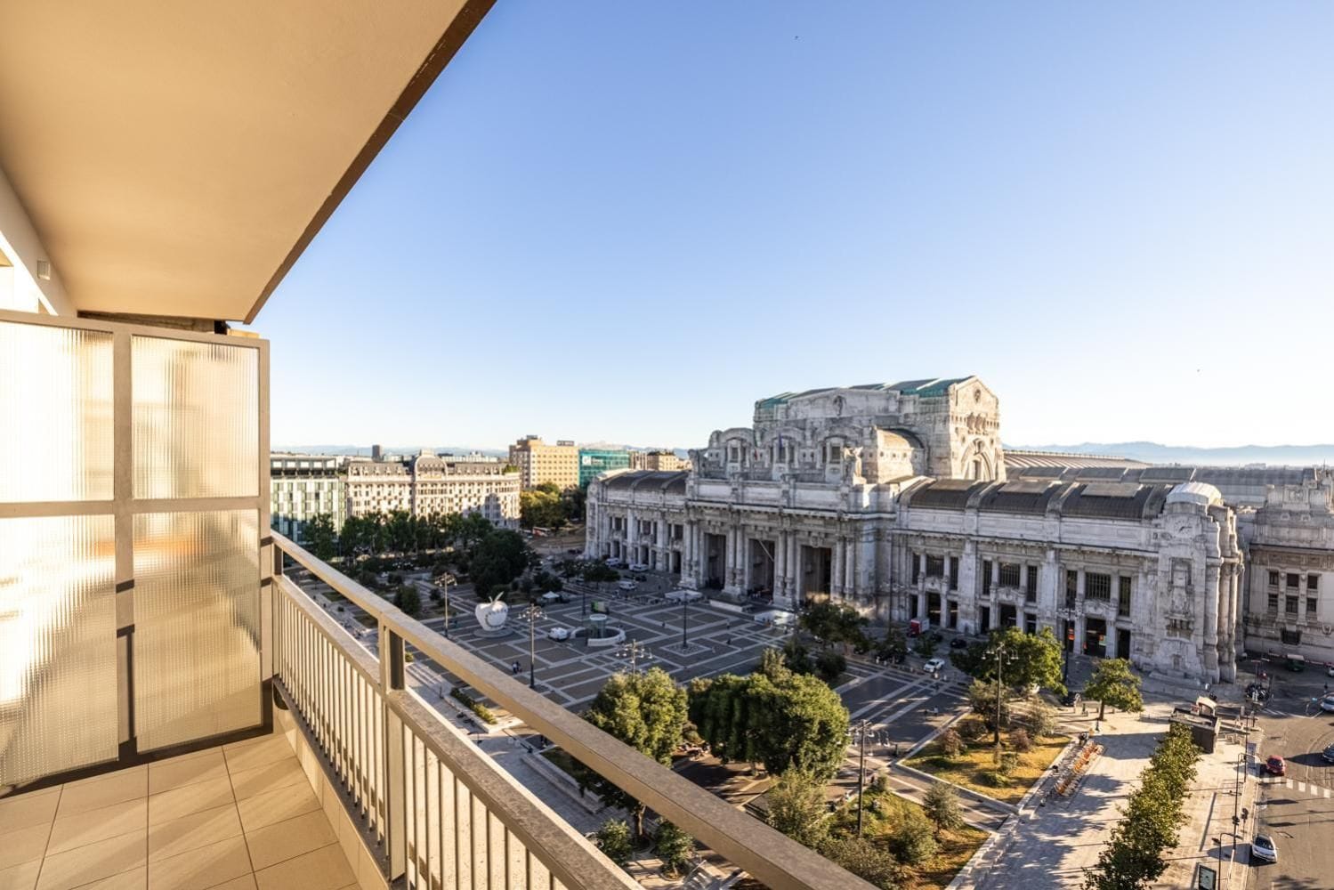 A view from a balcony overlooking a historic building with classical architecture, a spacious courtyard, and a clear sky.