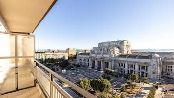 Une vue depuis un balcon donnant sur un bâtiment historique à l’architecture classique, une cour spacieuse et un ciel dégagé.