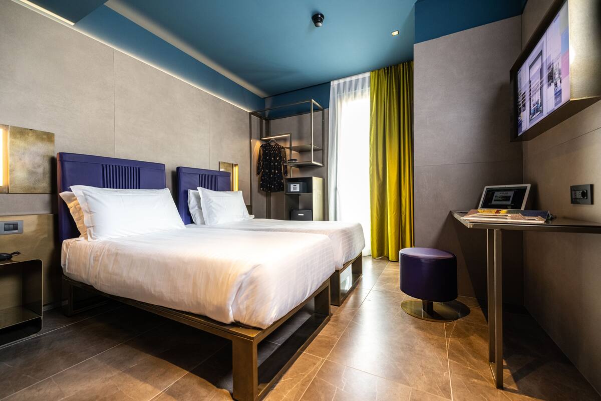 A modern hotel room with a large bed, a desk, and a TV on the wall.