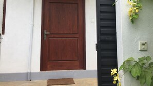 A wooden door with a decorative upper panel, a black gate, and a plant with yellow flowers. - Casa 44 - Karapitiya (Galle)