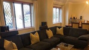 Una sala de estar con un sofá modular, una mesa de centro de vidrio y una zona de comedor con sillas y una mesa.