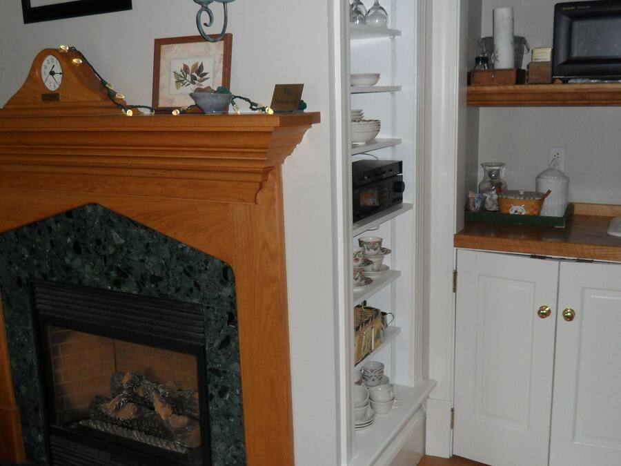 A living room with a fireplace, a wooden mantel, and a shelf with decorative items.