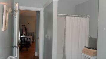 A room with a wooden floor, a white door, a white radiator, a white curtain, and a small table with a vase.