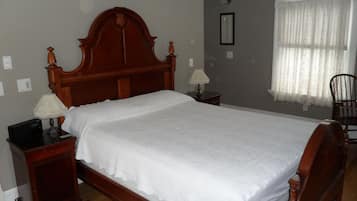 A bedroom with a wooden bed, two bedside tables, a lamp on each, a chair, and a window with curtains.