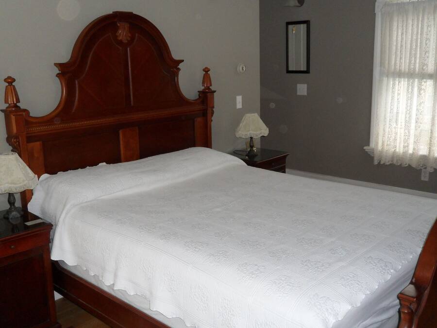 A bedroom with a wooden bed, two bedside tables, a lamp on each, a chair, and a window with curtains.
