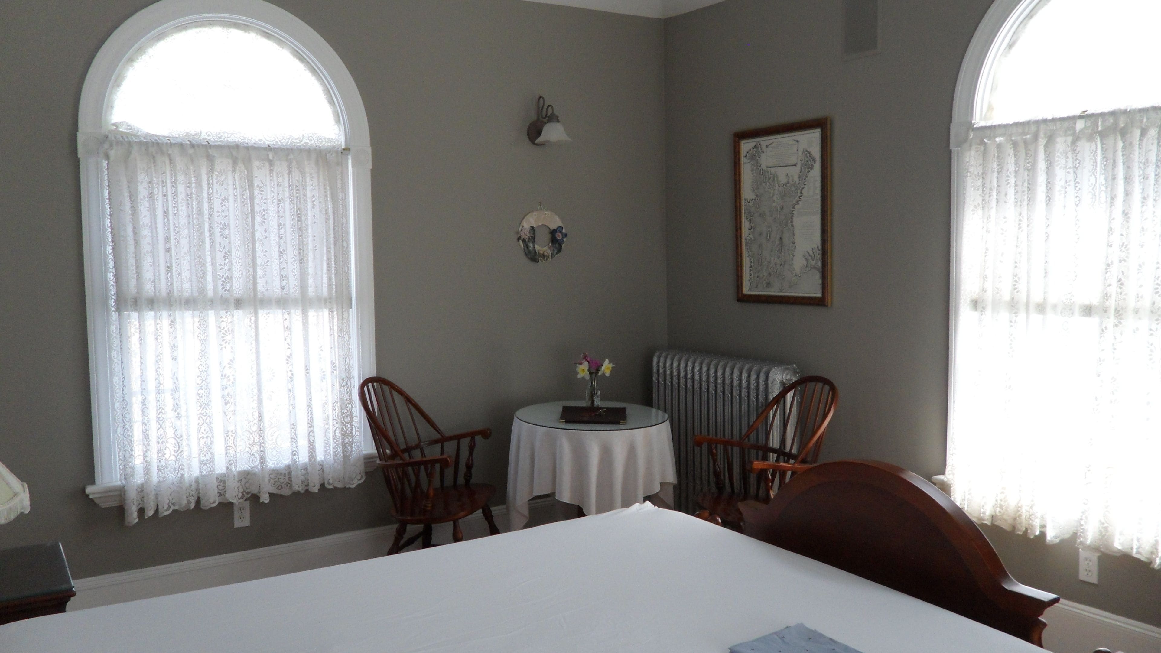 Une pièce avec deux chaises en bois, une petite table ronde, un radiateur et un tableau encadré accroché au mur.