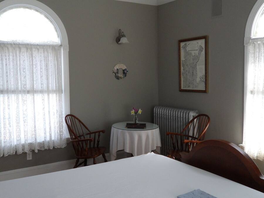 Une pièce avec deux chaises en bois, une petite table ronde, un radiateur et un tableau encadré accroché au mur.