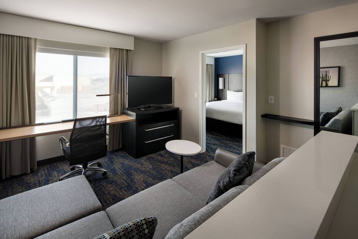 A hotel room with a sofa, a TV, a desk, and a bed.