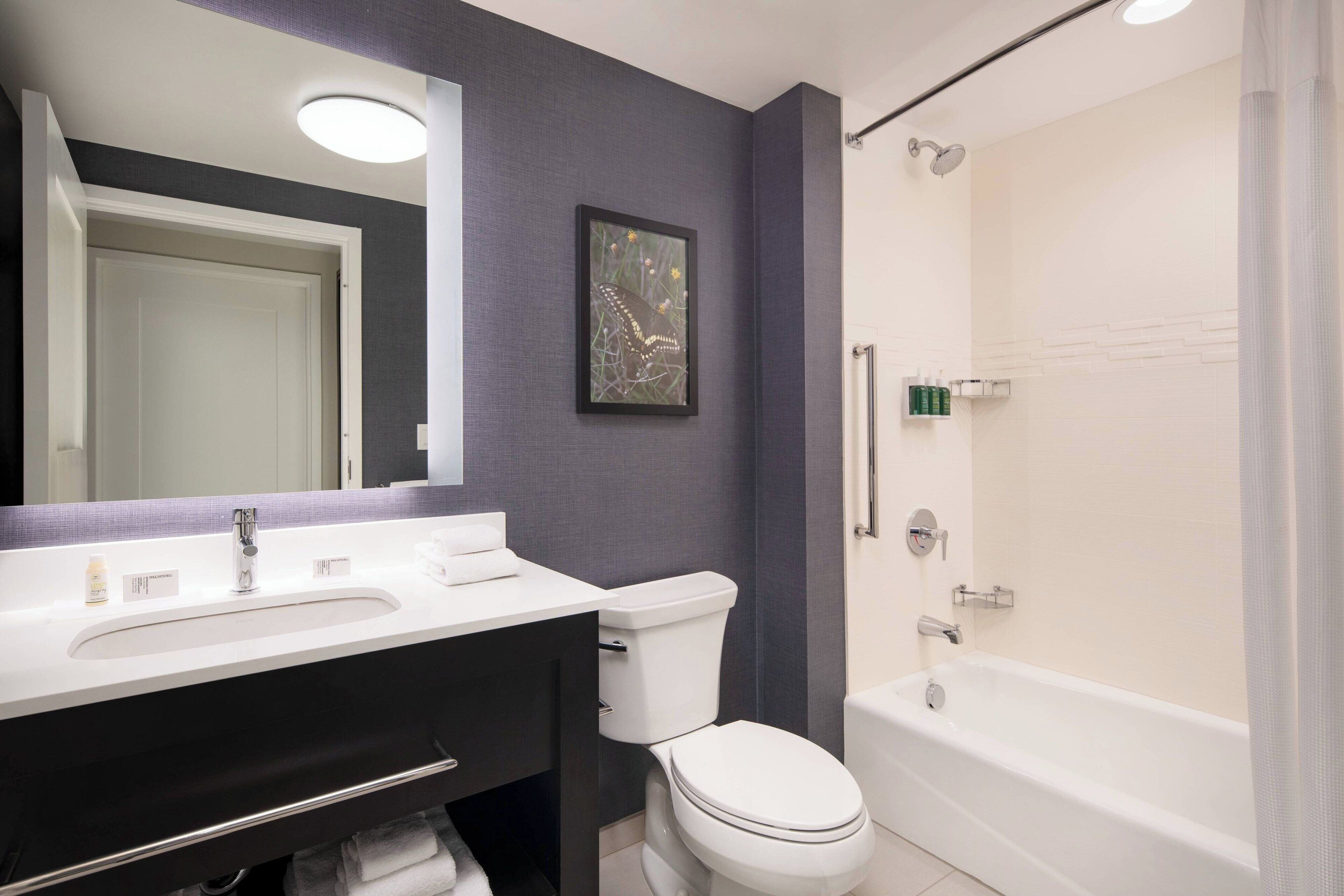 A bathroom with a white sink, toilet, and bathtub. There is a framed picture on the wall and a mirror above the sink.