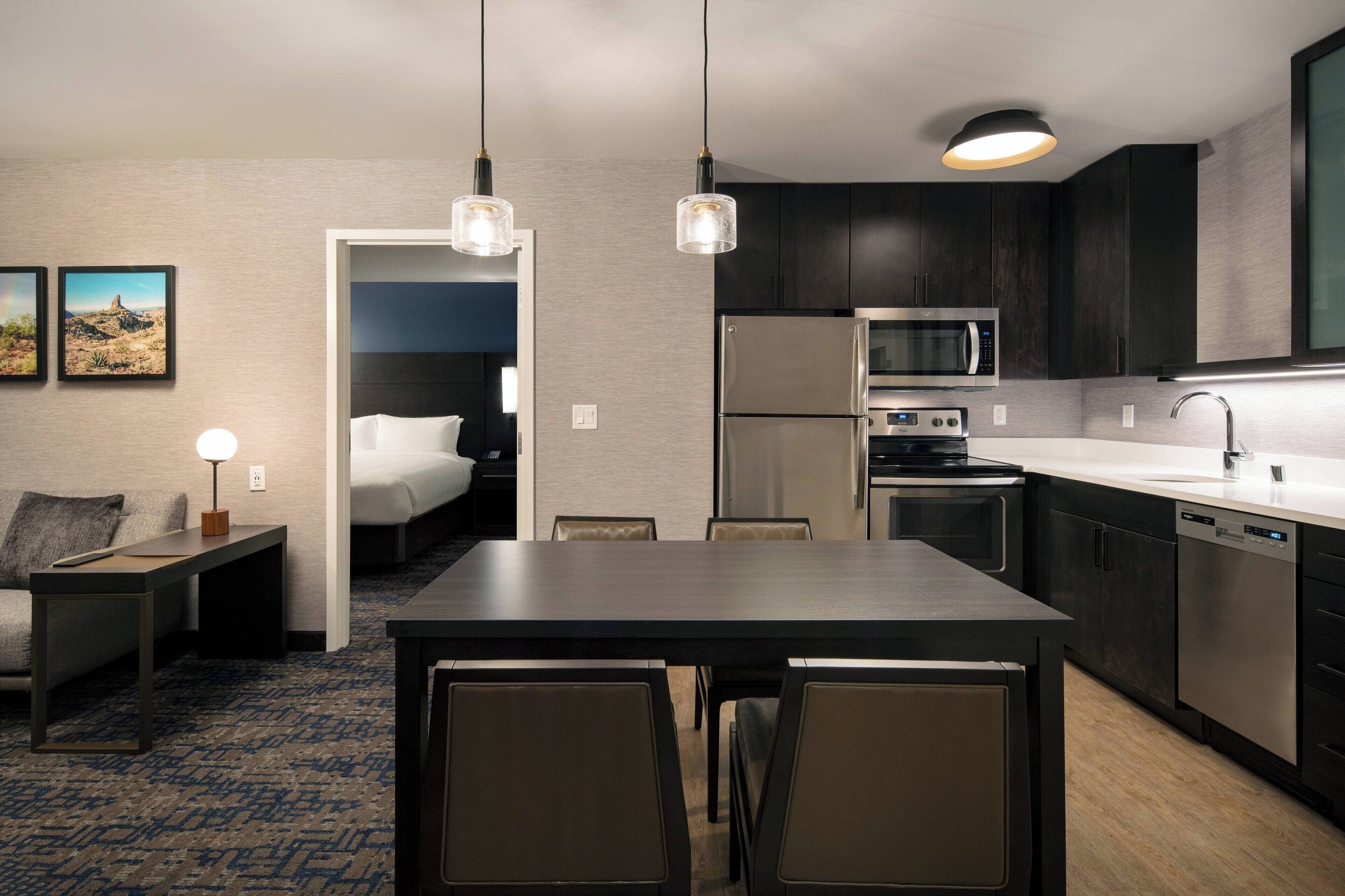 A modern hotel room with a kitchenette, a dining area, and a bedroom.