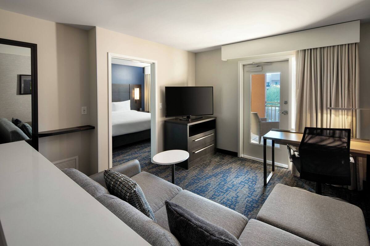 A hotel room with a sofa, a TV, a small table, a desk, and a bed.