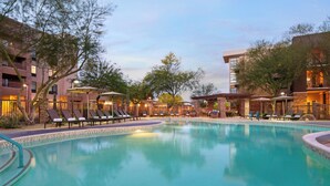 A swimming pool with lounge chairs and umbrellas, surrounded by buildings with balconies and outdoor seating areas. - Residence Inn Scottsdale Salt River (Scottsdale)