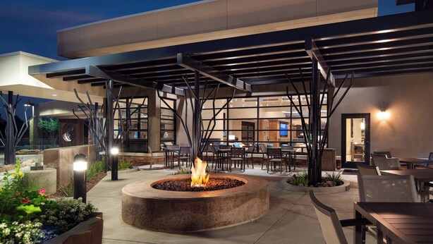 An outdoor patio area with a central fire feature, seating arrangements, and a covered walkway. - Residence Inn Scottsdale Salt River (Scottsdale)