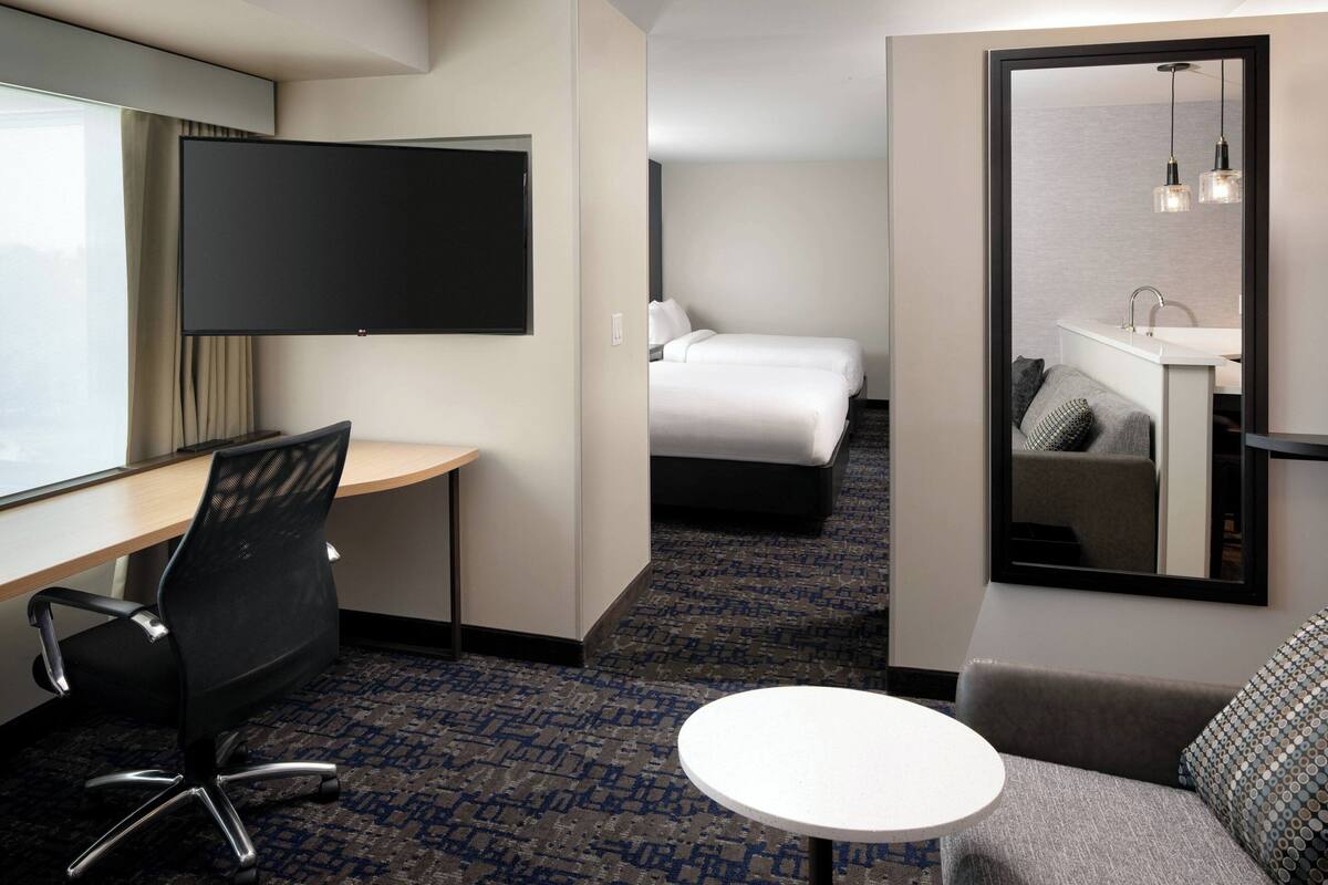 A hotel room with a desk, chair, bed, and a small round table.