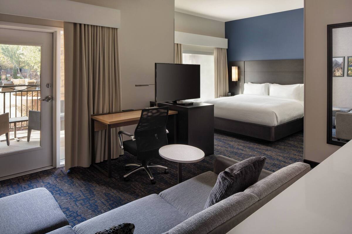 A hotel room with a bed, a desk with a TV, a sofa, and a small table.