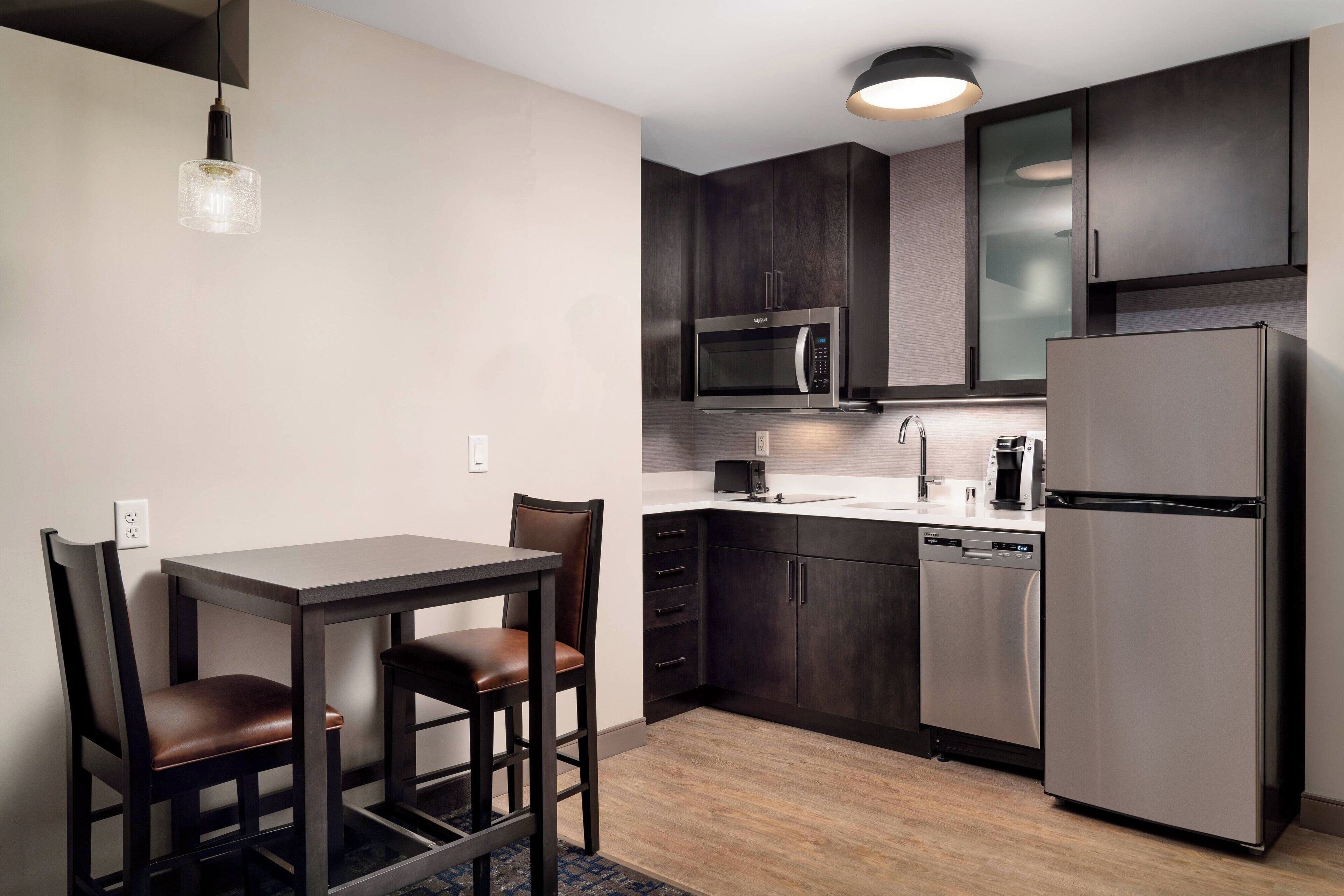 A modern kitchen with dark wood cabinets, stainless steel appliances, and a dining area with two chairs and a table.