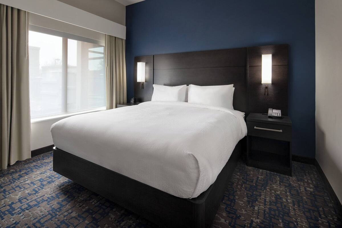 A hotel room with a large bed, a nightstand with a lamp, and a window with curtains.