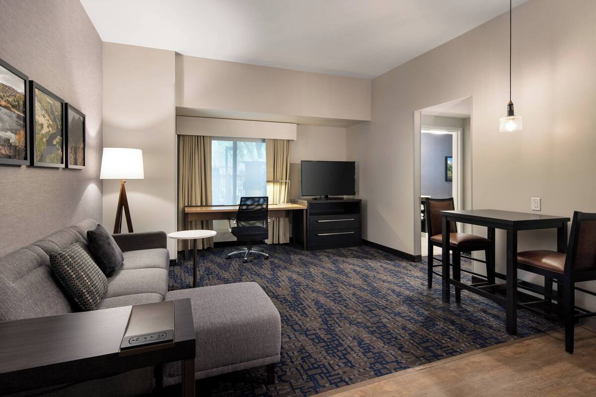 A hotel room with a sofa, a desk, a television, and a dining table.