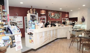 Un café avec un comptoir, des étagères remplies de divers articles et un espace pour s’asseoir.