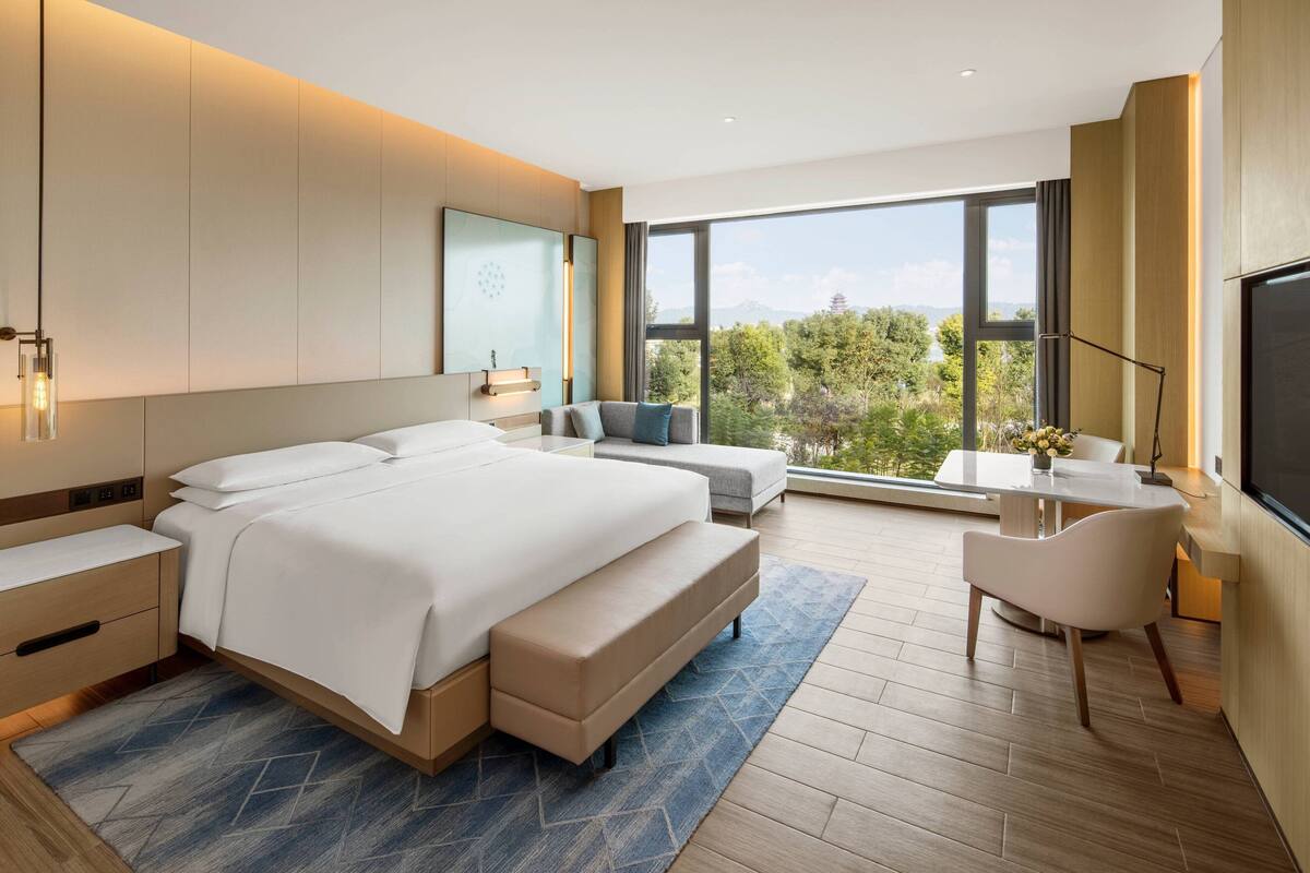 A modern hotel room with a large bed, a desk, and a view of the outdoors.