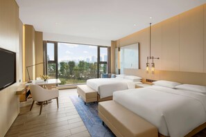 A modern hotel room with two beds, a desk, and a large window offering a city view.