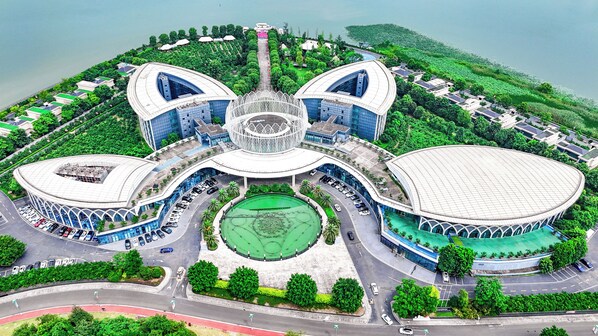 A large, modern building with a central atrium, surrounded by greenery and a body of water.