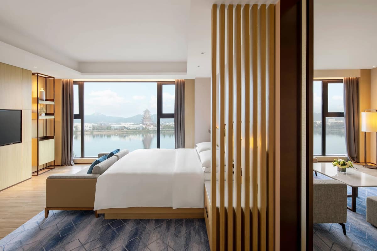 A modern hotel room with a large bed, a desk, and a view of a temple and water.