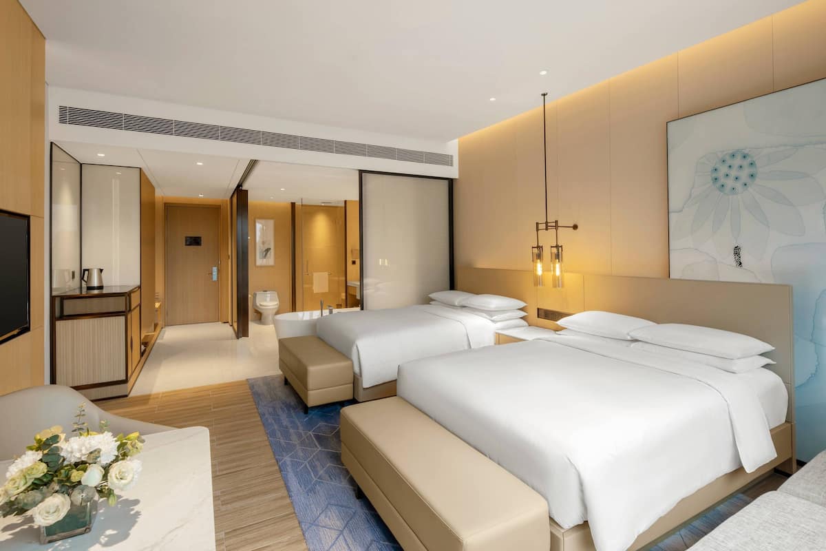A modern hotel room with two beds, a desk, a TV, and a bathroom.