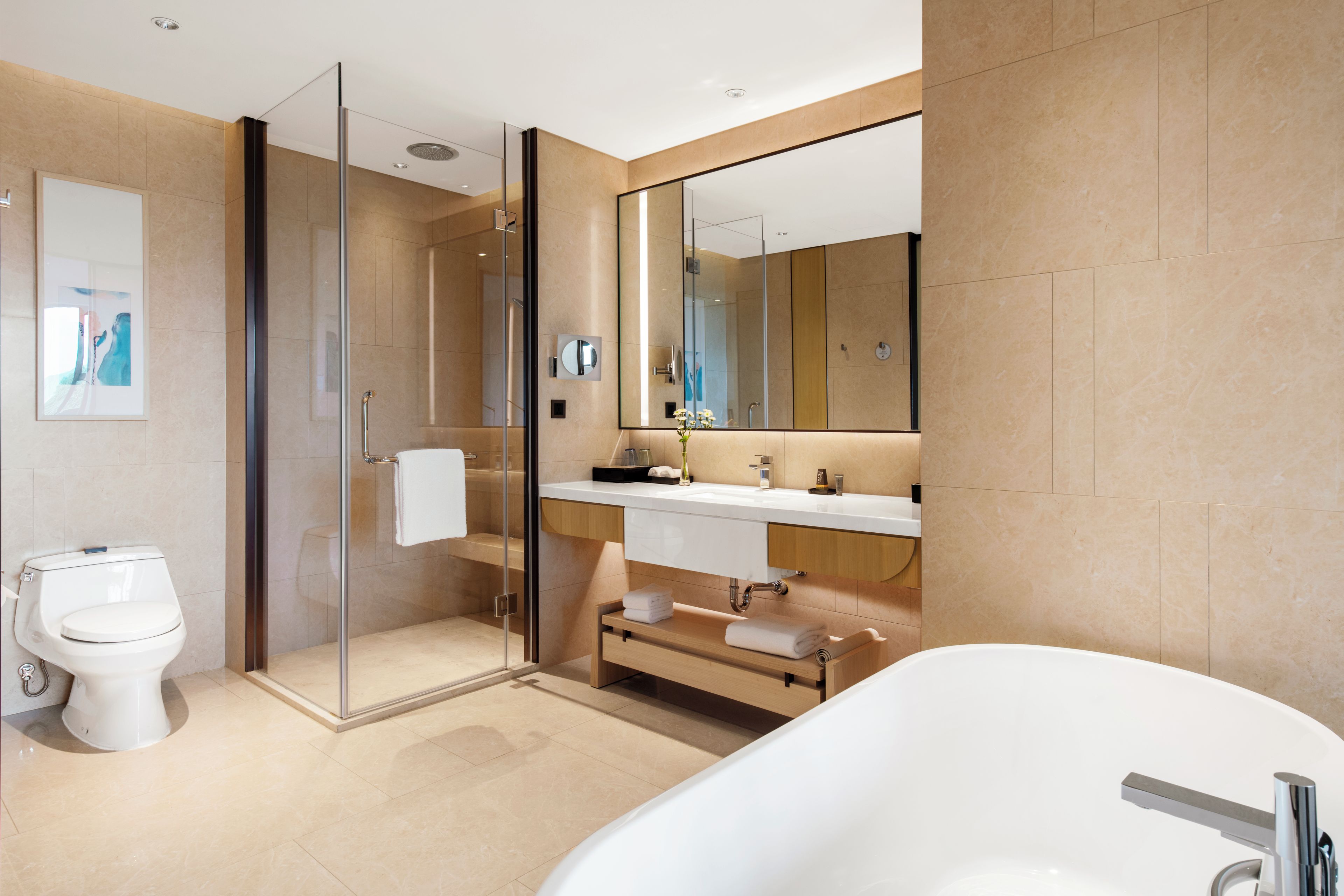 Un baño moderno con ducha envuelta en vidrio, inodoro blanco, espejo grande y bañera independiente.