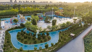 Luchtbeeld van een waterpark met meerdere glijbanen en zwembaden, omgeven door groen en een stadsachtergrond.