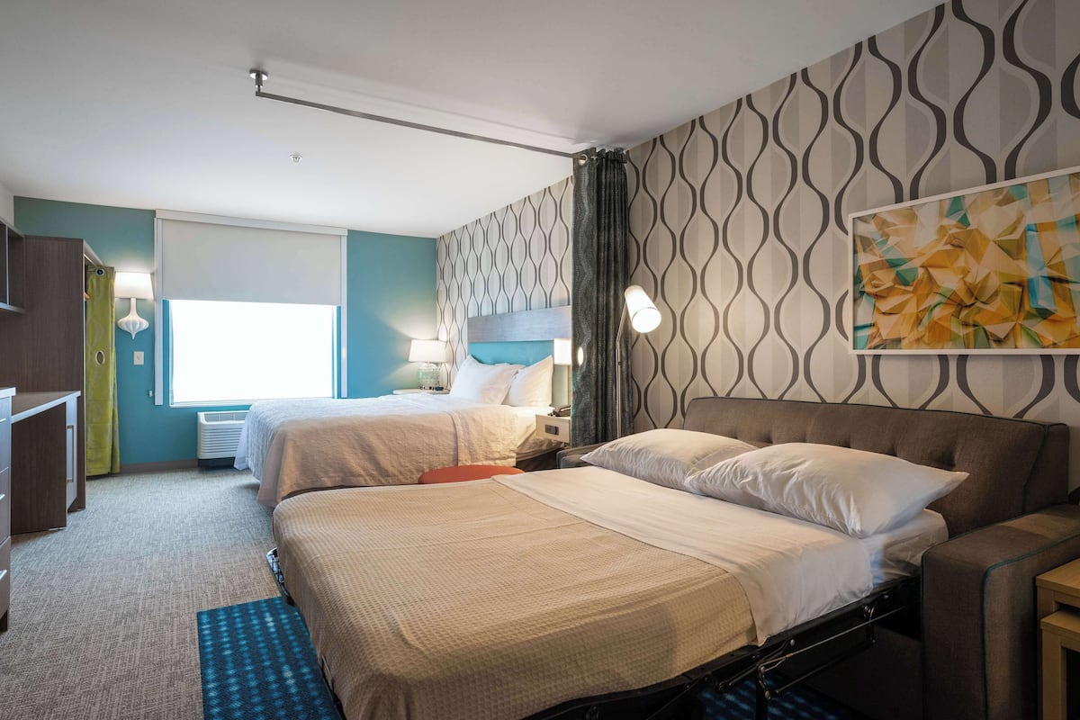 Une chambre d’hôtel avec deux lits, un bureau, une lampe et une fenêtre.