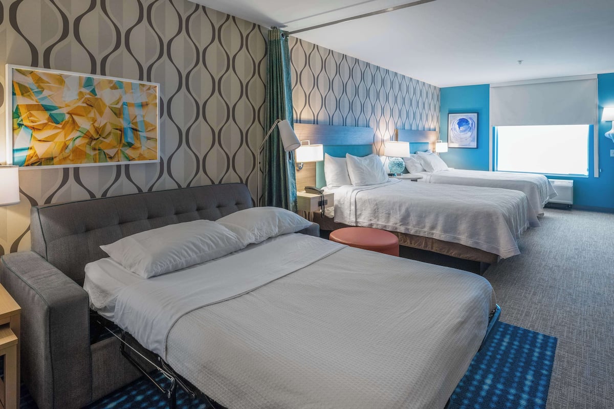 Une chambre d’hôtel avec deux lits, un canapé, un bureau et un grand tableau abstrait accroché au mur.