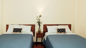 A hotel room with two beds, each with a blue bedspread and a geometric patterned pillow. There is a nightstand between the beds with a vase of flowers. - Hotel Rex (Toluca)