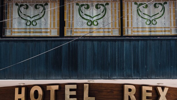 A hotel entrance with a sign reading "HOTEL REX" and decorative glass windows above. - Hotel Rex (Toluca)