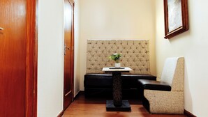 A corner room with a wooden door, a black bench, a small table with a plant, and a patterned wall. - Hotel Rex (Toluca)
