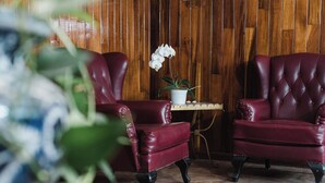 A room with two red leather armchairs, a small white table with a potted orchid, and a wooden wall. - Hotel Rex (Toluca)