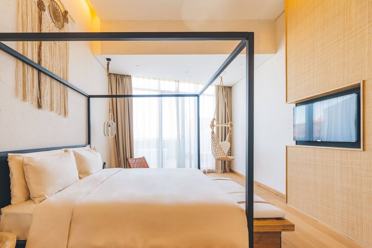 Ein modernes Hotelzimmer mit einem Himmelbett, einem Hängesessel und einem großen Fenster mit Vorhängen.