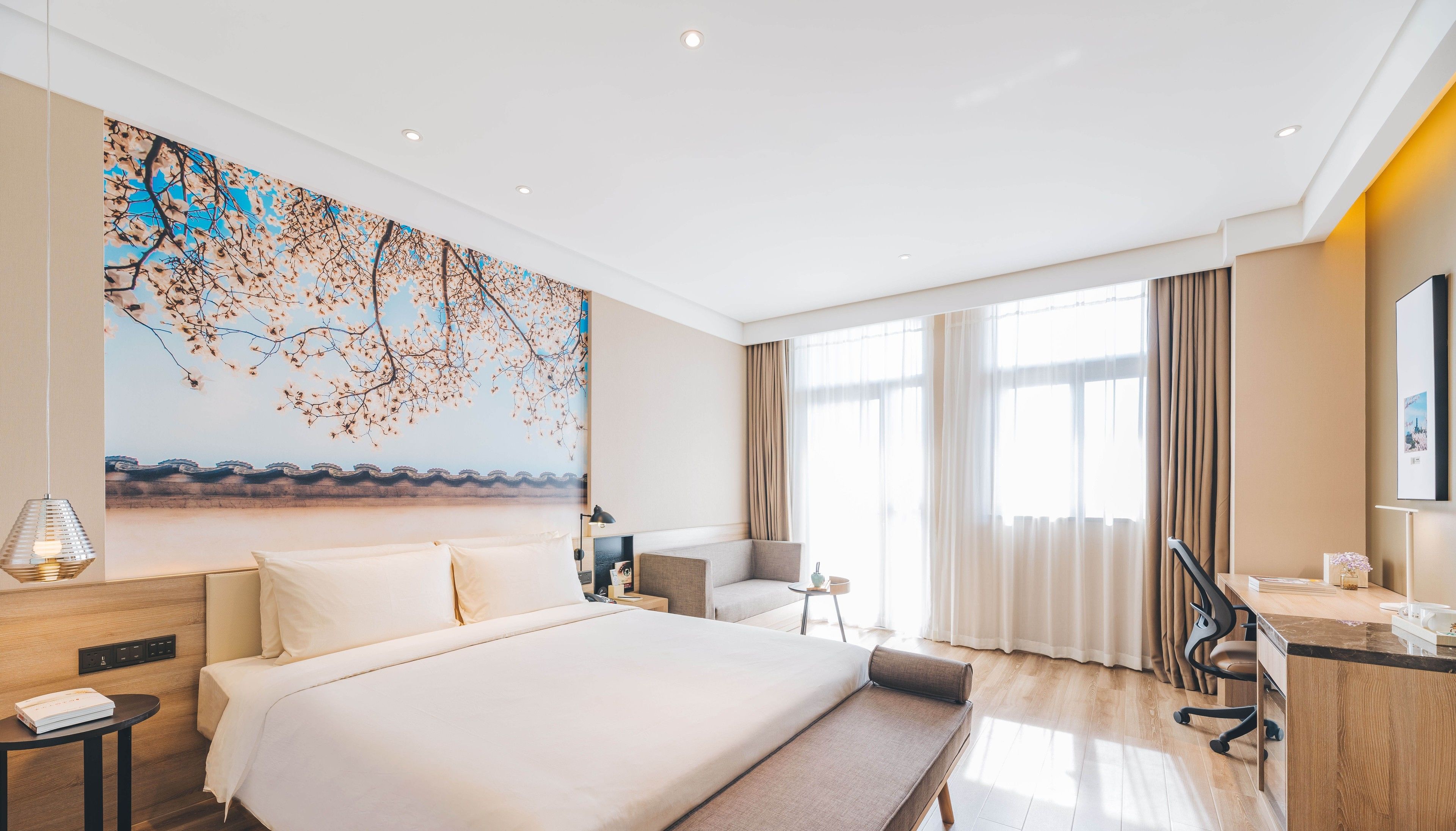 Une chambre d’hôtel moderne avec un grand lit, un bureau, une chaise et une grande fenêtre avec des rideaux.