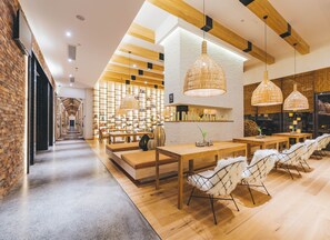 A modern interior with a long hallway leading to a seating area with tables and chairs, wooden beams on the ceiling, and a brick wall on one side. - Atour Hotel Dianchi Kunming (Kunming)