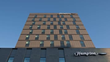 A tall, modern building with the 'Hampton by Hilton' sign on the top.