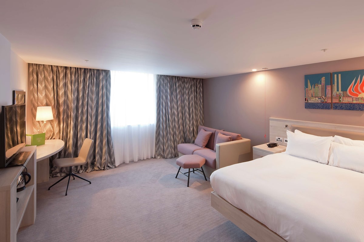 A hotel room with a bed, a desk with a chair, a sofa, and a painting on the wall.