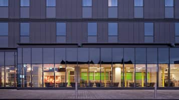 Een modern gebouw met grote ramen en een groen verlicht interieur, mogelijk een hotel of kantoor.