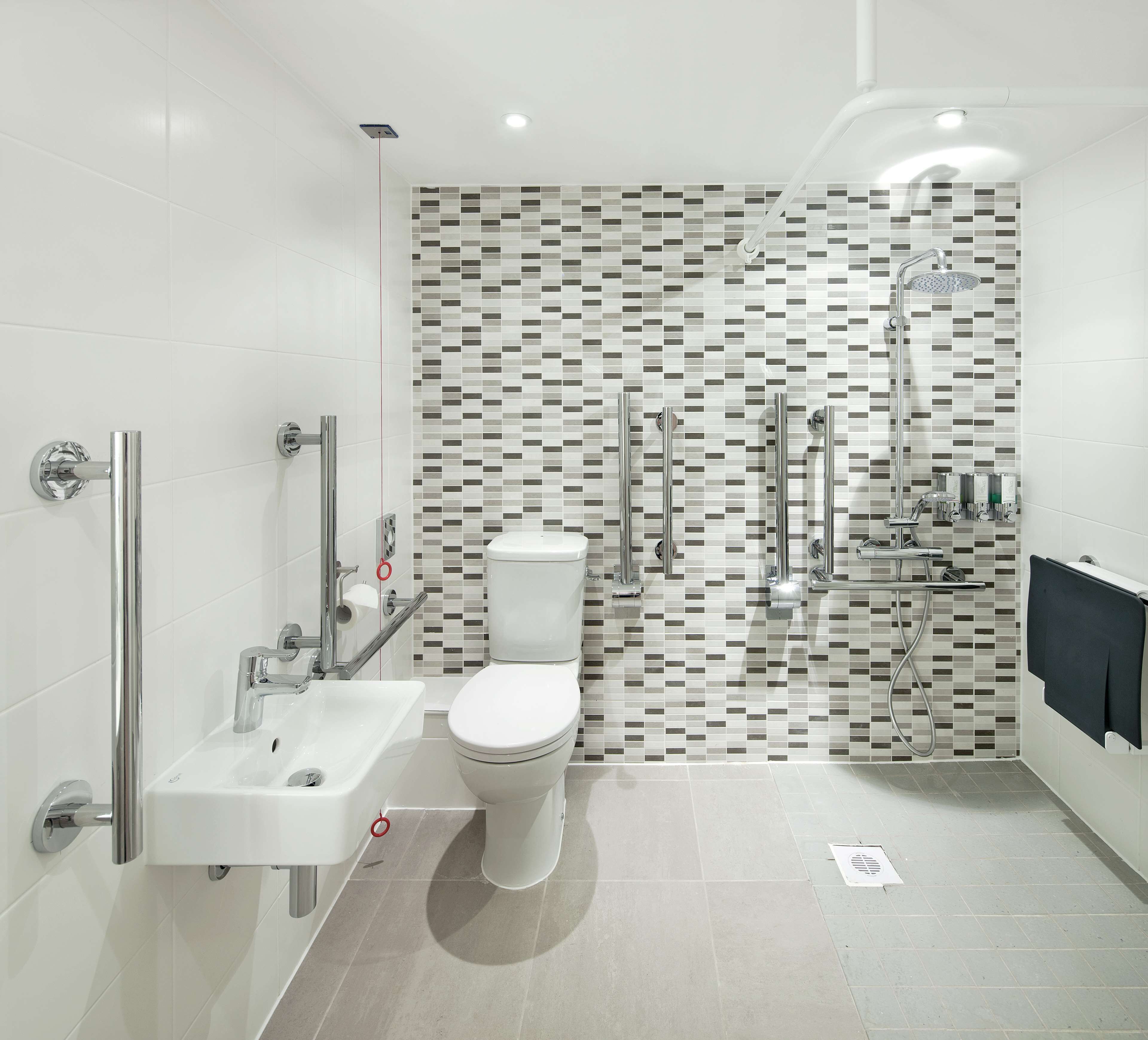 Un baño moderno con lavamanos, inodoro y zona de ducha blancos.