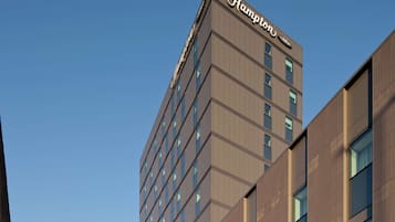 A modern hotel building with a prominent 'Hampton' sign at the top.