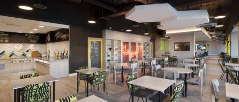 A modern restaurant with multiple seating areas, including tables and chairs, and a kitchen visible in the background.