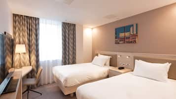 A hotel room with two beds, a desk, a lamp, and a painting on the wall.
