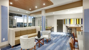 A modern hotel lobby with a blue carpet, a beige sofa, and a small table with chairs. - Holiday Inn Express Kermit by IHG (Kermit)