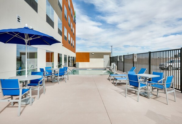 An outdoor patio with blue chairs and tables, a pool, and a building with multiple windows and a wheelchair-accessible sign.