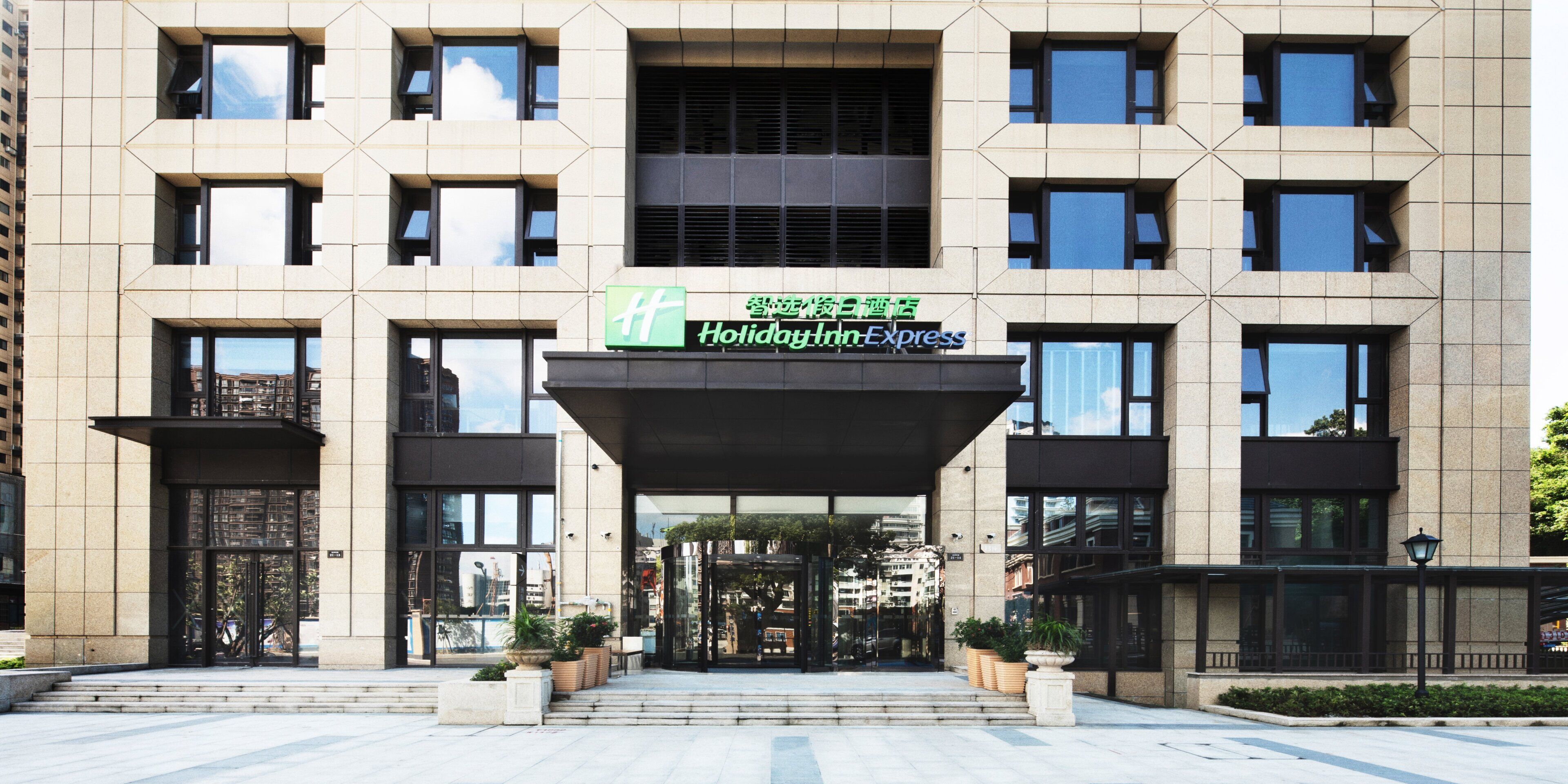Entrada de hotel con diseño moderno, destacando un amplio frente de vidrio y el letrero de Holiday Inn Express.
